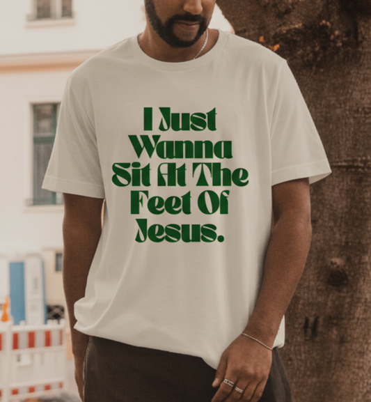 Man wearing a white t-shirt with green text standing outdoors next to a tree.