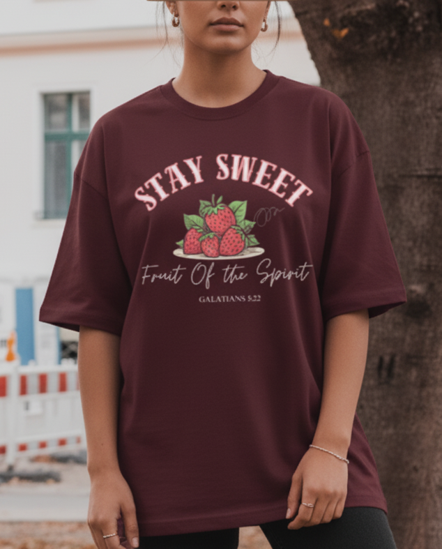 Person wearing a maroon t-shirt with a strawberry graphic and text in an urban setting